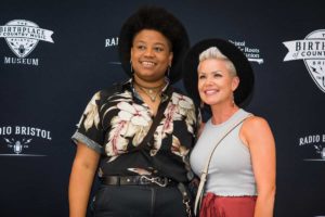 Amythyst Kiah wearing a Hawaiian-style shirt and black hat with a fan wearing a similar hat.
