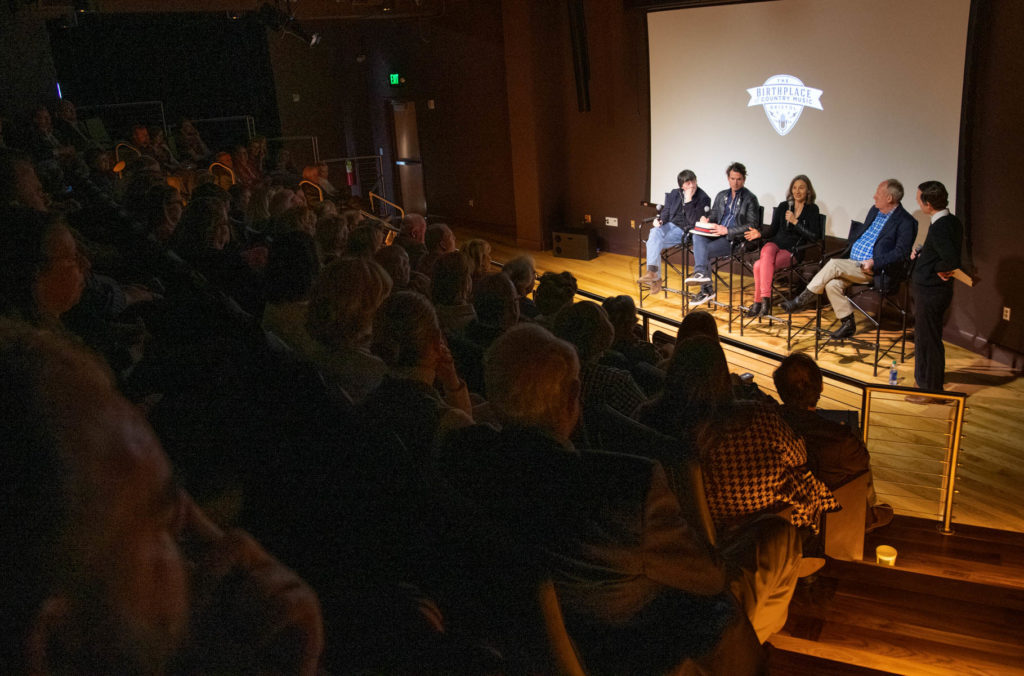 A view of the Q&A panel from the back of the room showing the crowded theater with the listening audience.