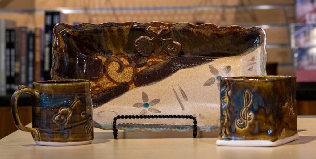 Photo of a ceramic tray with flower designs and a crossed banjo and guitar with musical themed mug and flower vase.
