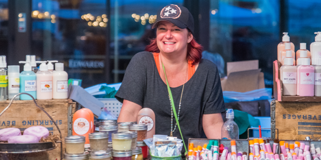 Vendor at For the Love of Suds booth, surrounded by lotions, soaps, and many other bath and body products.