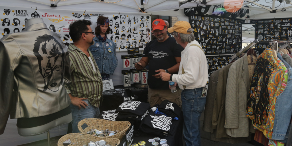 View into the Status Graphics booth showing customers looking at t-shirts, graphics, and decals.