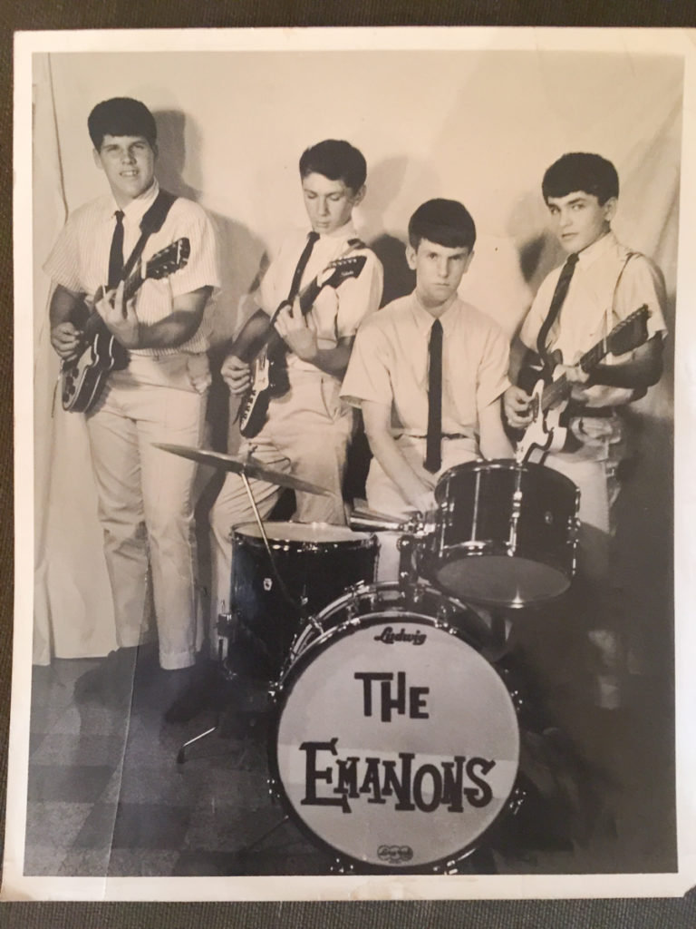 Four young musicians with their instruments, including their drum set bearing the band name, The Emanons.