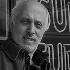 Black-and-white photograph of Colin Escott, an older white man wearing a dark shirt/jacket and in front of what appears to be a neon sign.