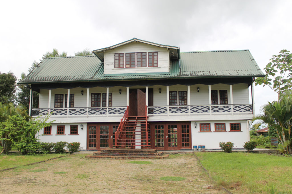 A two-storey, with gable, plantation house, reconstructed. It is white with red stairs and doors on the ground floor, and a green roof.