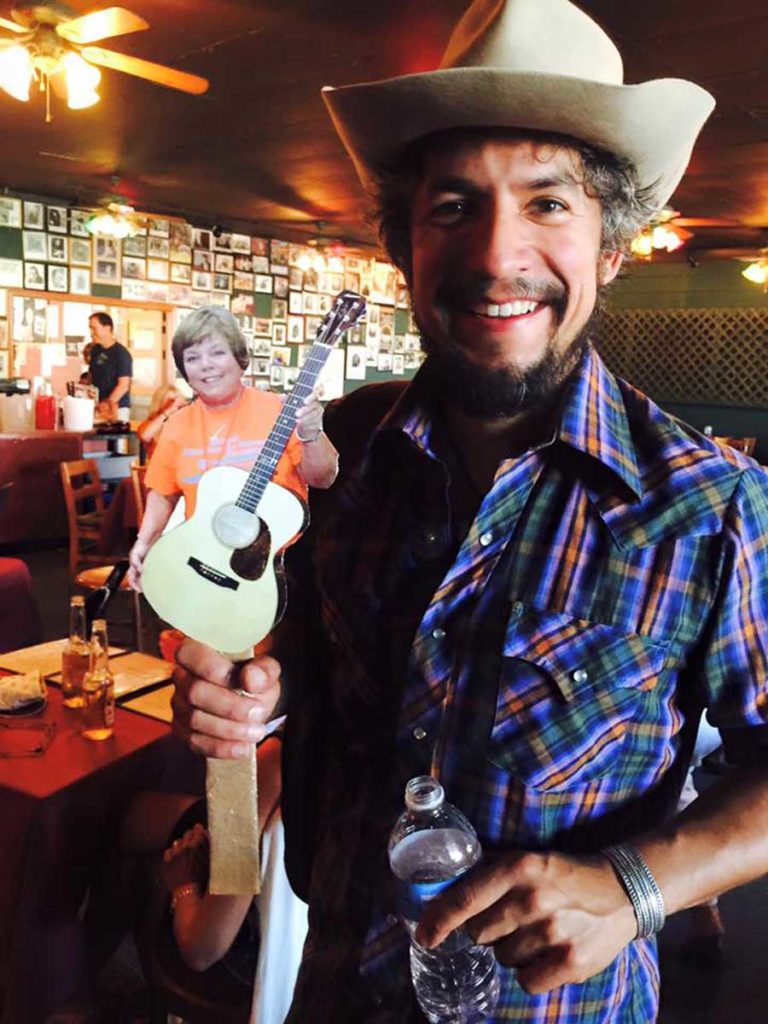 Cruz Contreras of The Black Lillies holding up a "flat Leah" - a little poster sized image of Leah on a stick.
