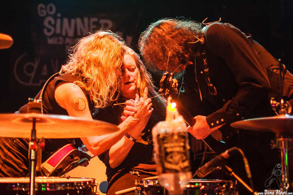 Three Dead Moon band members grouped around the drums during a live performance.