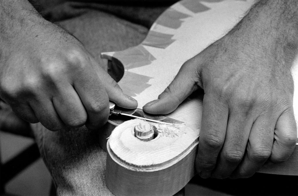 Black-and-white image with a close up of two hands carving the body of a mandolin.