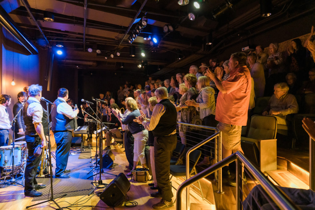 Davina and the Vagabonds on stage in front of the Farm and Fun Time crowd, all on their feet and clapping enthusiastically.