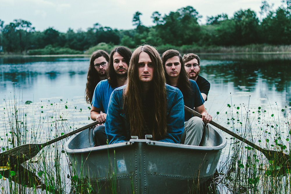 Photo of the band all sitting in a row boat on a small pond.