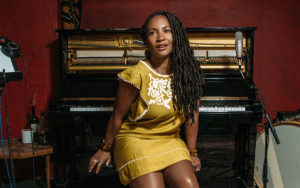 A photo of Miko Marks sitting on a bench in front of a piano.