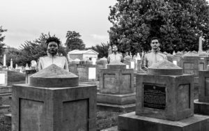 A photograph taken in a cemetery. Three of the band's members are scattered about, posing behind the headstones.