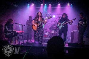 The bandon stage with a multitude of colored lights shining down on them, coalescing into a purpse aura. 
