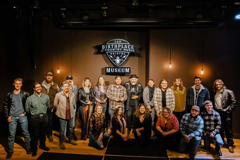 20 competing songwriters in the 2023 Bristol qualifying round standing under the Birthplace of Country Music Museum sign in the performance theater of the museum.