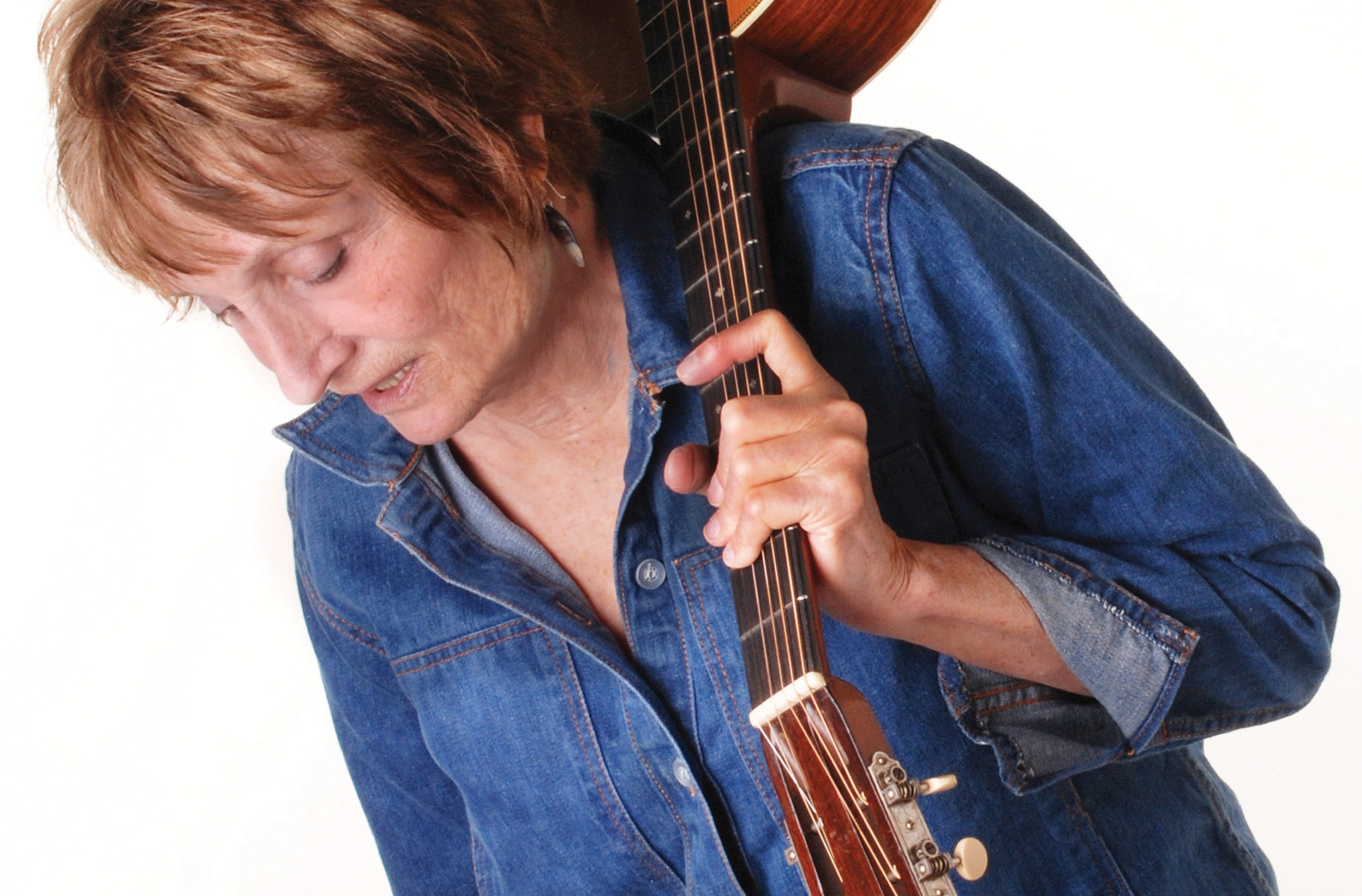 A photo of Alice Gerrard with and acoustic guitar slung over her shoulder.