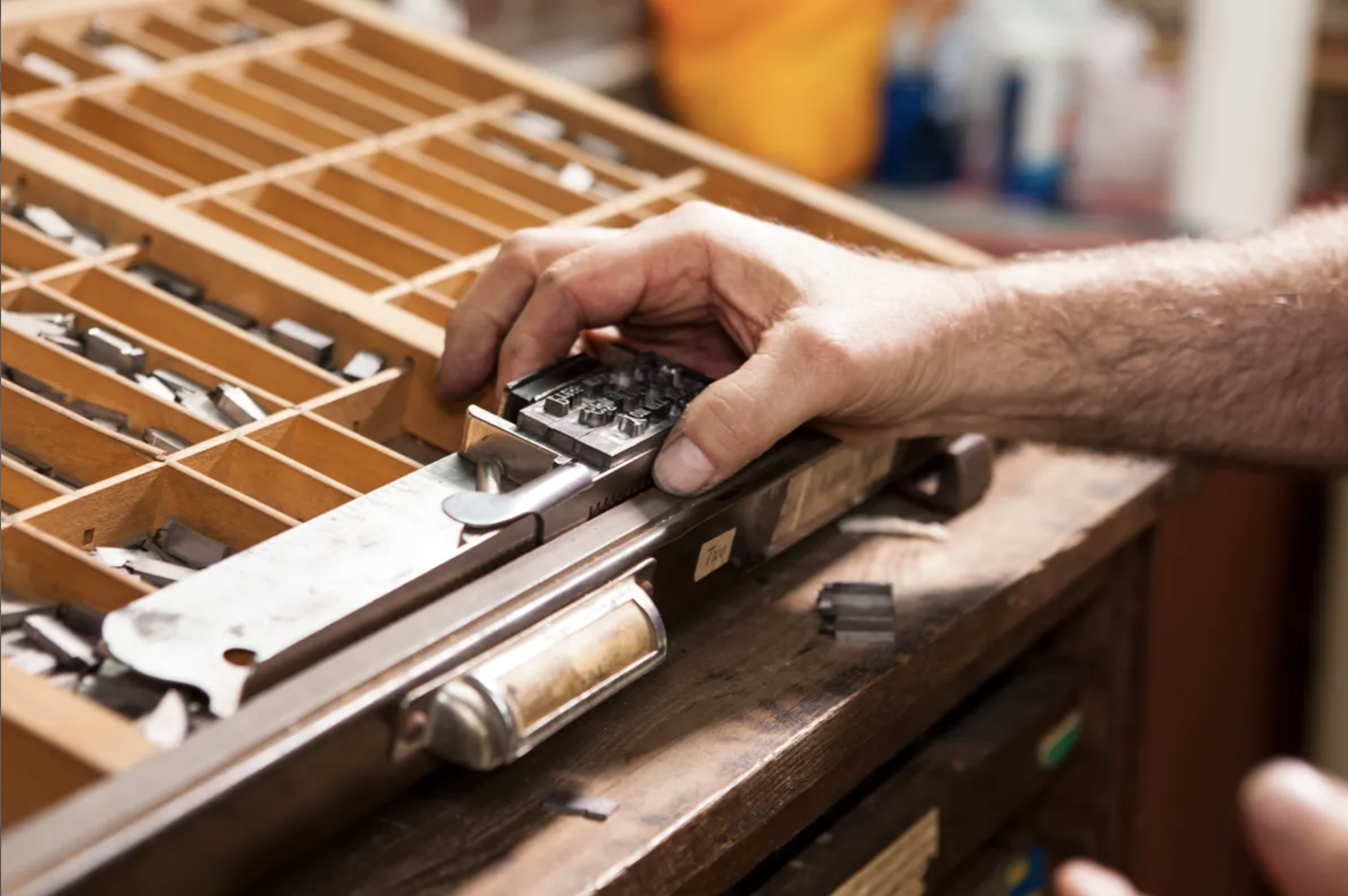 A closeup of a right hand is holding metal typeface letters.