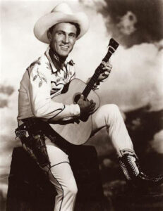 Singer and actor Ken Curtis, posing in a white cowboy outfit and holding a guitar.